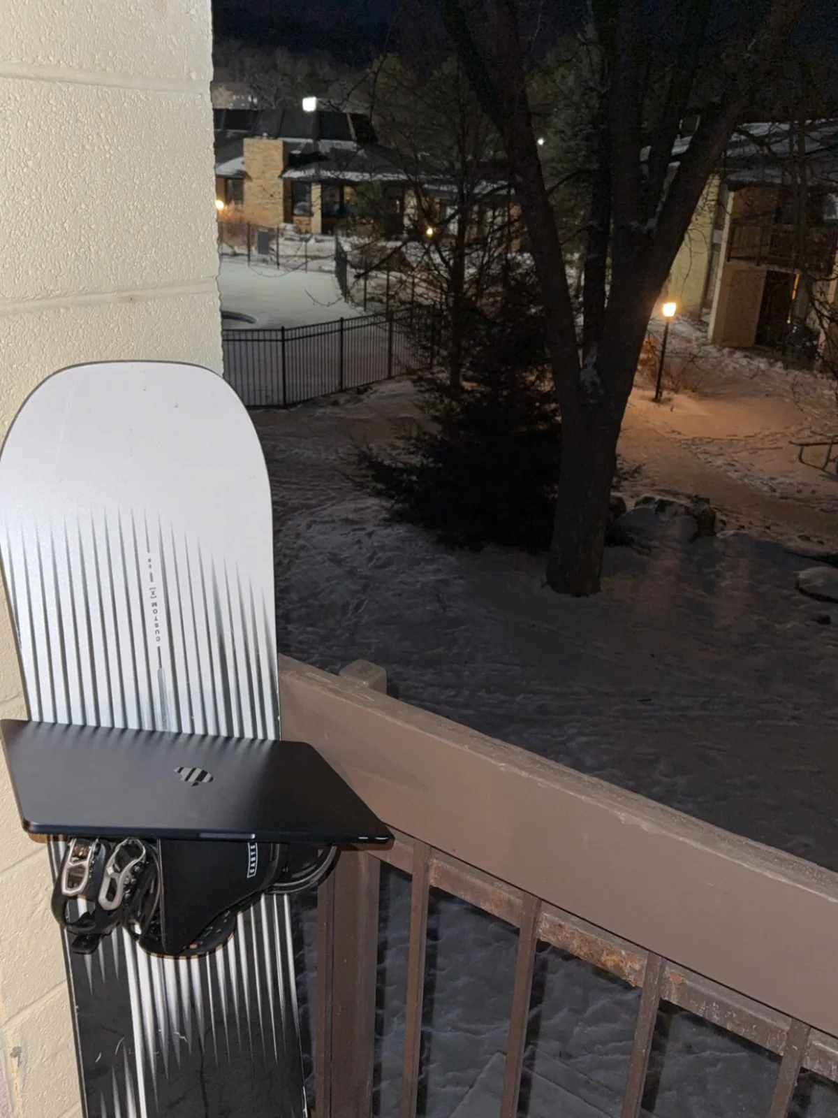 A closed laptop resting on a snowboard beside a snowy balcony