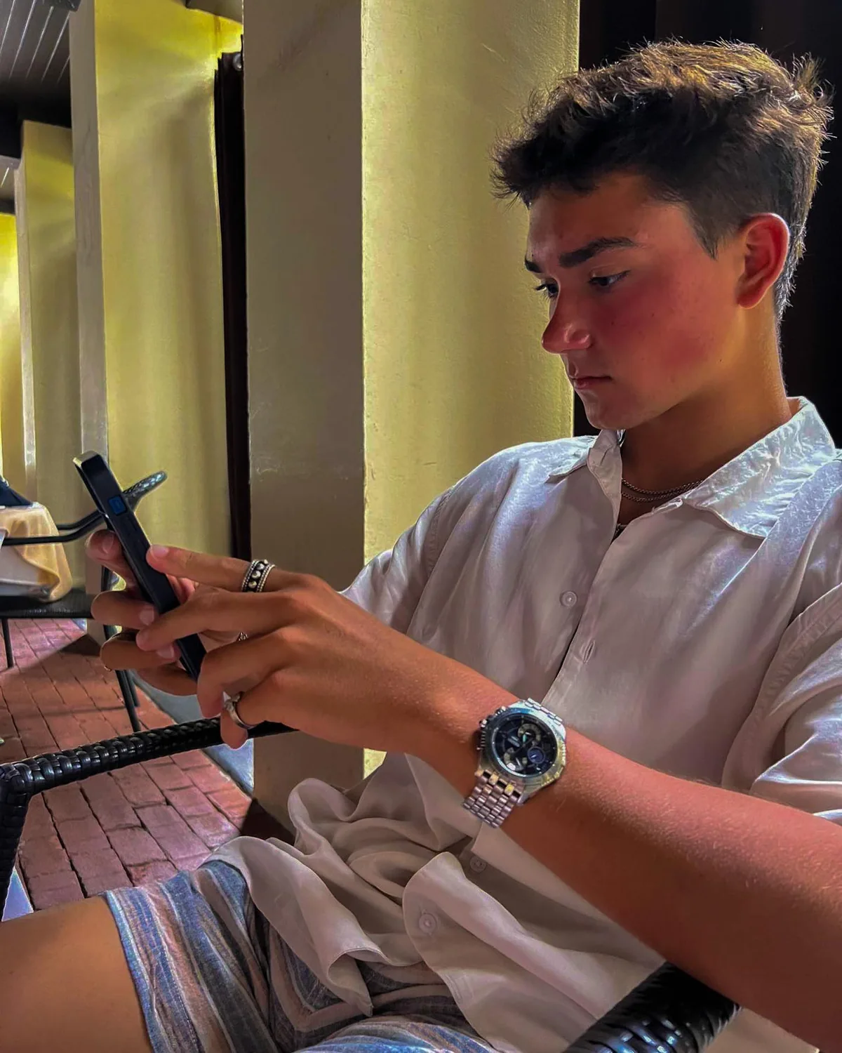 Alex looking at a phone while seated beside a column