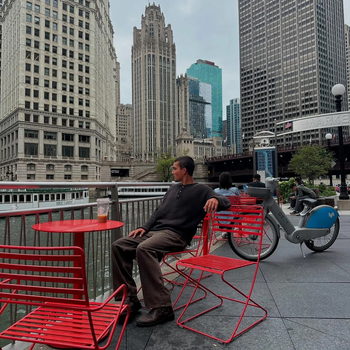 Seated beside the river among red chairs and city buildings